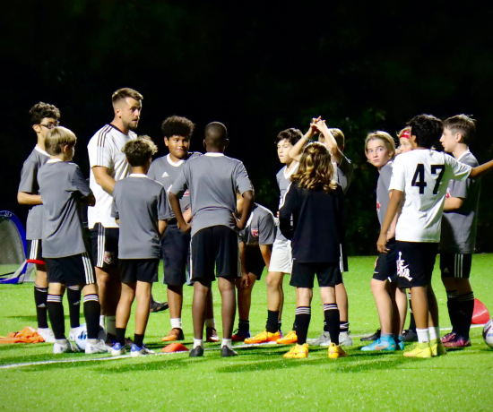 A football coach talks to a team of young players on a football pitch